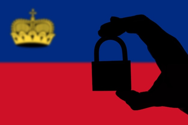Segurança de Liechtenstein Silhueta de mão segurando um cadeado sobre a bandeira nacional