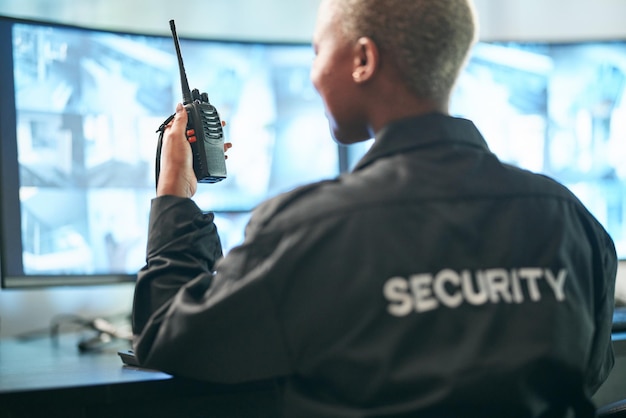 Segurança de volta e vigilância por rádio com uma mulher oficial em um controle para monitorar a atividade criminosa Despacho de segurança e CCTV com uma guarda feminina sentada em seu escritório usando um walkie talkie