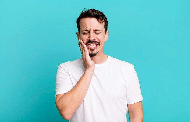 Segurando a bochecha e sofrendo dor de dente dolorosa, sentindo-se doente, miserável e infeliz, procurando um dentista