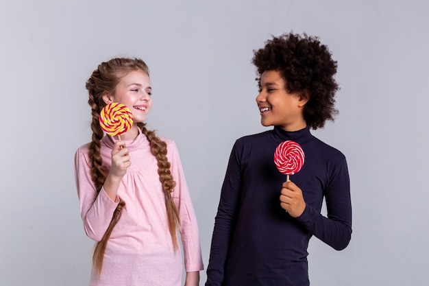 Foto segurando doces coloridos. crianças bonitas e alegres se divertindo na plataforma e posando para o cinegrafista