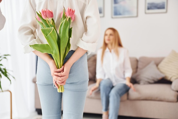 Segurando flores jovem mãe com sua filha está em casa durante o dia