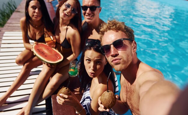 Segurando melancia Grupo de jovens felizes se divertem na piscina durante o dia