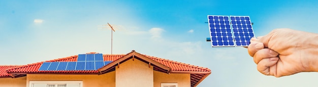 Foto segurando o painel solar na frente de uma instalação de casa fotovoltaica