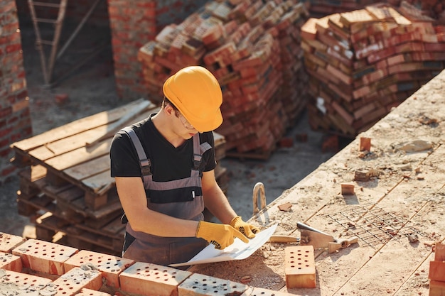 Segurando o plano nas mãos Trabalhador da construção civil em uniforme e equipamento de segurança tem trabalho na construção