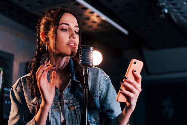 Segurando o smartphone Jovem bela artista feminina ensaiando em um estúdio de gravação