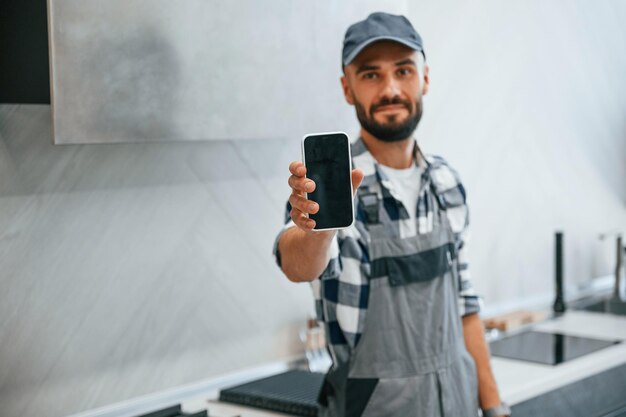 Foto segurando o smartphone na mão o encanador de uniforme está dentro de casa