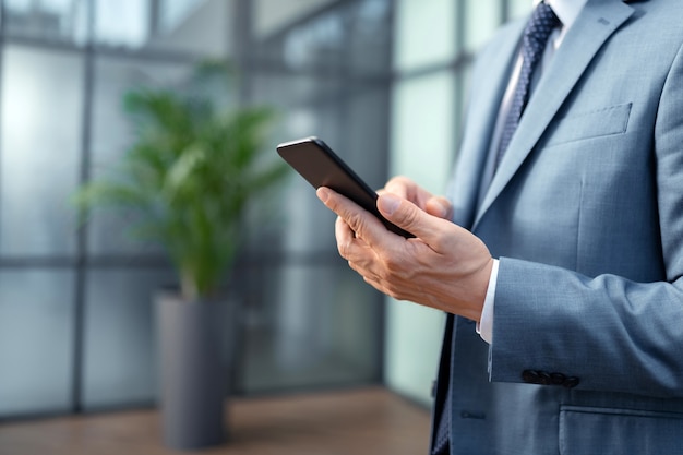 Foto segurando um smartphone preto. perto de um empresário vestindo um terno cinza, segurando um smartphone preto e digitando uma mensagem