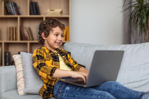 Seguridad cibernética para niños Joven niño emocionado escribiendo en una computadora portátil explotando internet en el espacio libre de casa