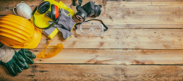 Seguridad en la construcción Casco protector auriculares guantes y gafas en pancarta de fondo de madera