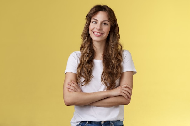 Seguro, despreocupado, alegre, sonriente, profesional, profesional, brazos cruzados, pecho, seguro de sí mismo, pose, posición, cómodo, camiseta blanca, sonriente, dentudo, encantado, stand, amarillo, fondo, amistoso