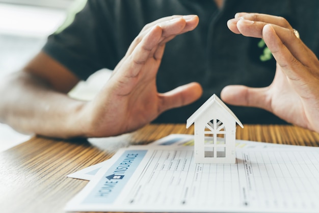 Seguro del hogar o protección de la propiedad. Agente de seguros completo, casa modelo de madera sobre el dinero.