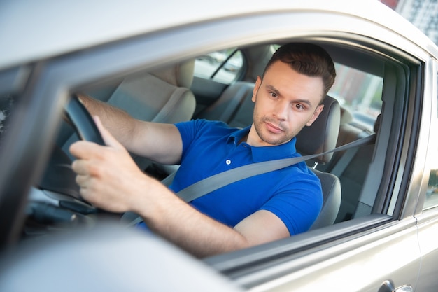 Foto seguro de joven apuesto hombre exitoso está conduciendo su coche moderno