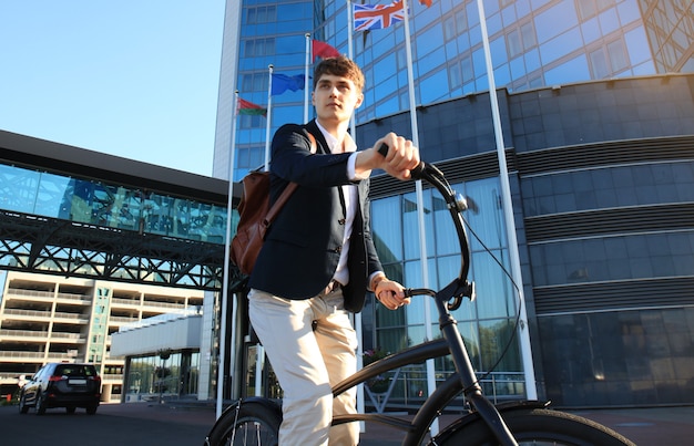 Seguro joven empresario caminando con bicicleta en la calle de la ciudad.