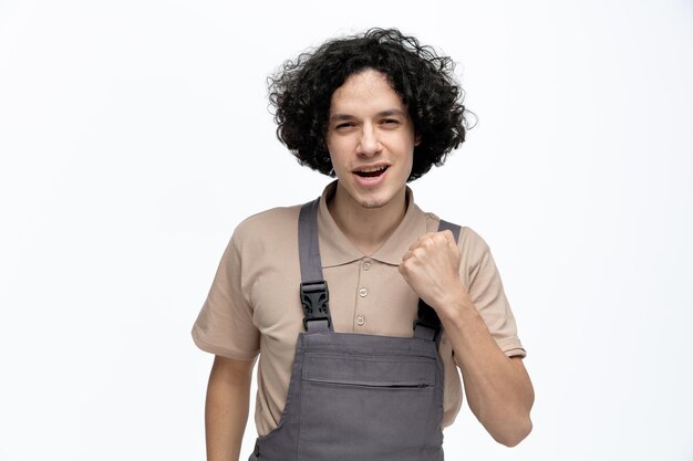 Seguro joven trabajador de la construcción masculino vistiendo uniforme mirando a la cámara haciendo sí gesto aislado sobre fondo blanco.