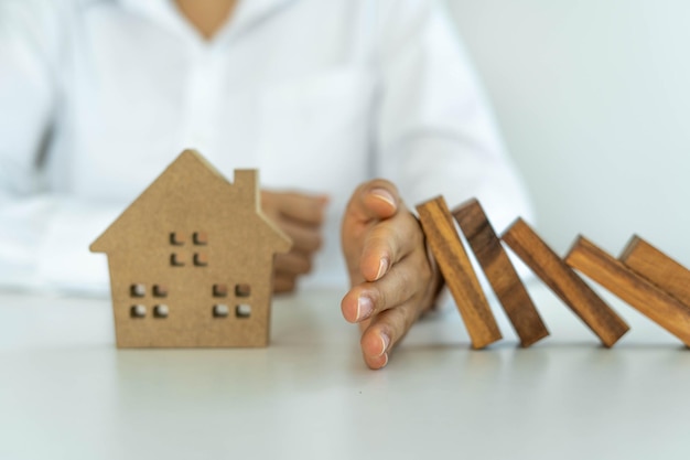 Foto el seguro con las manos protege una casa el bloque de dominó de madera está a punto de caer sobre la casa seguro de hogar o concepto de seguro de casa