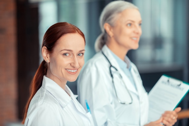 Seguro médico. Bela jovem médica ruiva sorridente com um jaleco branco ao lado de seu colega