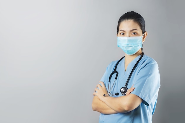Foto seguro de médico cirujano femenino asiático en uniforme azul con mascarilla protectora de pie con los brazos cruzados