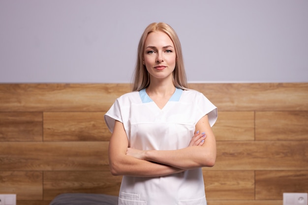 Seguro médico mujer o enfermera posando en ropa blanca, concepto sanitario. Mujer rubia se encuentra con los brazos cruzados aislado en la habitación del hospital