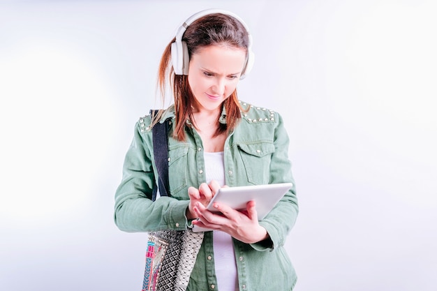 Seguro de sí mismo hermosa joven sobre fondo blanco vistiendo ropa casual y auriculares mirando la tableta del trabajo