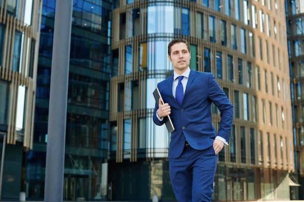 Seguro de sí mismo joven empresario exitoso con portátil moderno que va a la reunión al aire libre