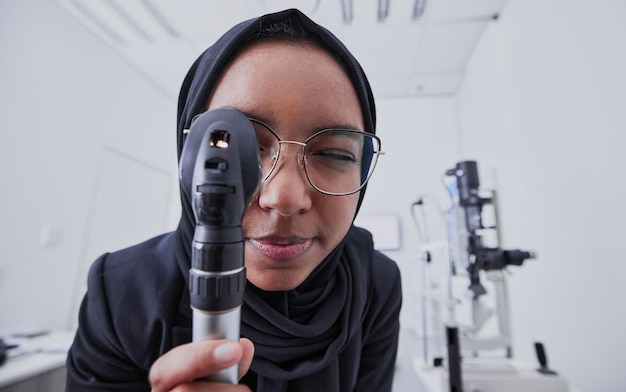 Sehoptiker und Frau mit Retinoskop im Krankenhaus zur Untersuchung Sehtest im Gesundheitswesen und muslimischer Arzt oder Augenarzt mit Ausrüstungswerkzeug für Augenpflege, Gesundheit und Wohlbefinden in der Klinik