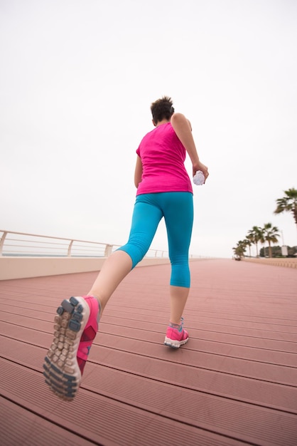 Sehr aktive junge schöne Frau, die damit beschäftigt ist, auf der Promenade am Meer entlang zu laufen, um ihre Fitness so gut wie möglich aufrechtzuerhalten