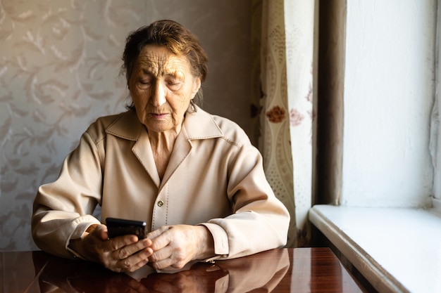 Sehr alte Frau benutzt ein Smartphone im Haus.