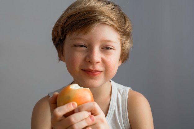 Sehr glücklicher Junge, der lächelt und einen reifen roten Apfel isst