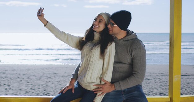 Sehr glückliches verliebtes Paar, das am Herbsttag Selfie am Strand macht