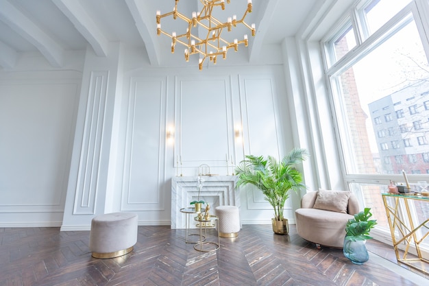 Sehr helles und helles Interieur des luxuriösen gemütlichen Wohnzimmers mit schicken, weichen beigefarbenen Möbeln mit goldenen Metallelementen, riesigem Fenster zum Boden und Holzparkett