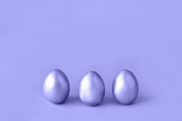 Sehr Peri. Farbe des Jahres 2022. Violette, violette Farben. Einfarbig. Ostereier auf blauem Hintergrund. Drei goldene Eier. Minimaler Stil. Osterdekorationen.