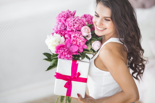 Sehr schöne Frau mit Blumen und Geschenk drinnen