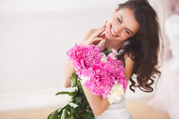 Sehr schöne junge Frau mit Blumen. Portrait des attraktiven Mädchens mit Pfingstrosen