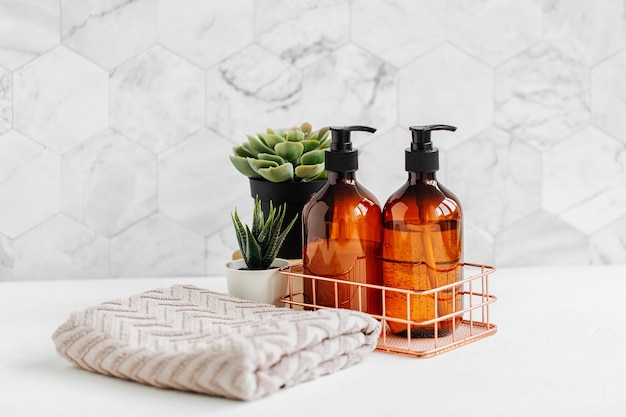 Seifen- und Shampooflaschen und Baumwollhandtücher mit grüner Pflanze auf weißem Tisch in einem Badezimmerhintergrund.