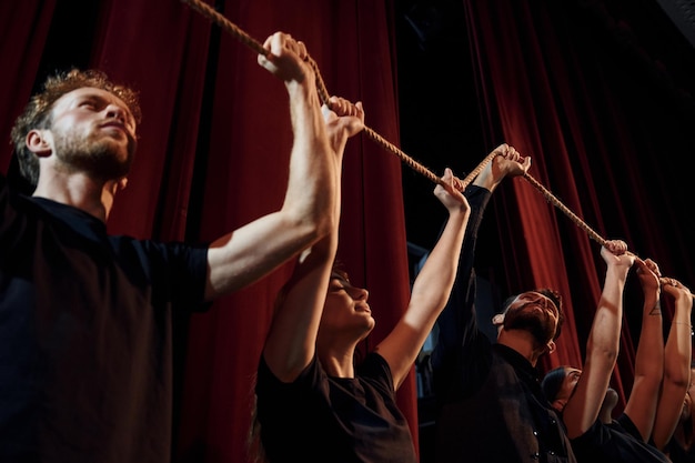 Seil in den Händen über den Köpfen halten Gruppe von Schauspielern in dunkler Kleidung bei der Probe im Theater