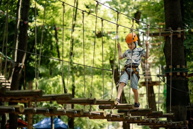 Seilpark für Kinder. Ein kleiner Junge in einer Klappe klettert auf Hindernisse. Aktive sportliche Erholung des Kindes.