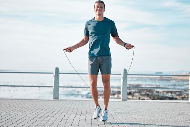 Seilspringen glücklich und Mann Training am Strand für sein Outdoor-Morgentraining und Fitness-Routine Athlet Cardio und männliches Springen am Meer oder am Meer für Wellness-Lifestyle