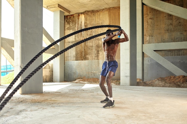 Seiltraining Sportler, der Kampfseile im Freien macht Schwarzer männlicher Athlet, der funktionelles Fitnesstraining mit schwerem Seil durchführt