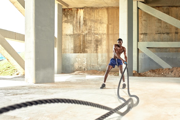 Seiltraining Sportler, der Kampfseile im Freien macht Schwarzer männlicher Athlet, der funktionelles Fitnesstraining mit schwerem Seil durchführt