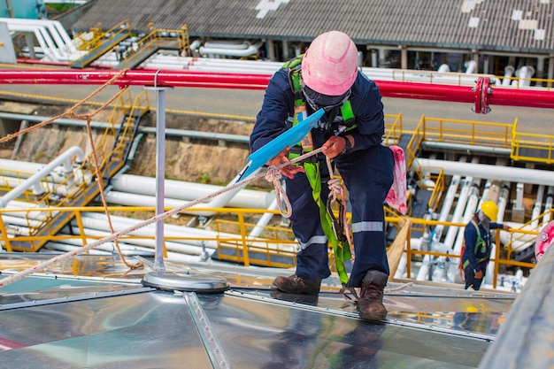 Seilzugangshöhensicherheit für männliche Arbeiter, die mit einem Knotensicherheitsgurt verbunden sind, der in die Absturzsicherungs- und Absturzsicherungs-Ankerpunktsysteme des Dachs einrastet, die zum Aufsteigen der Öltankkuppel auf der Baustelle bereit sind
