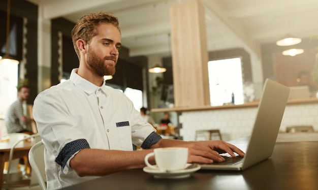 Sein perfektes Arbeitsumfeld Aufnahme eines jungen Mannes, der in einem Café einen Laptop benutzt