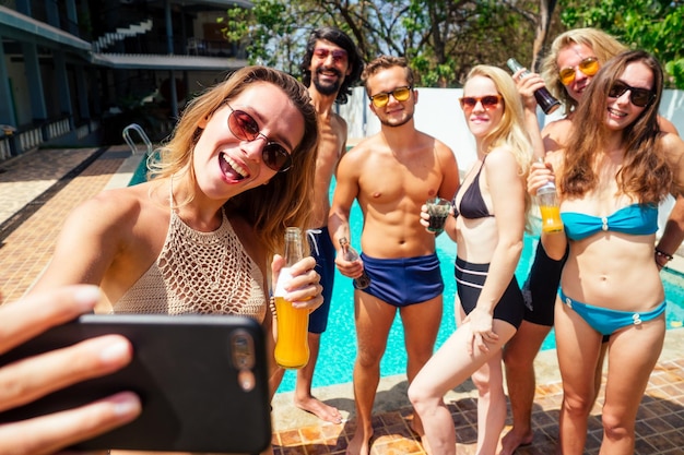 Seis amigos atraentes fazendo autoretrato no smartphone na piscina