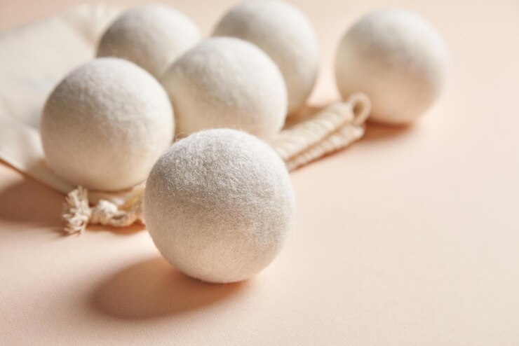 Seis bolas de secado de lana natural en una superficie suave de color beige acompañadas de una bolsa de cordón de algodón