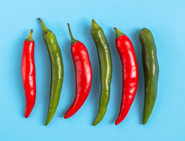 Seis chiles picantes de color rojo y verde yacen en fila sobre un azul claro