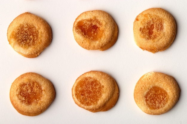 Seis galletas artesanales con mermelada de albaricoque dispuestas en filas uniformes aisladas sobre fondo blanco.