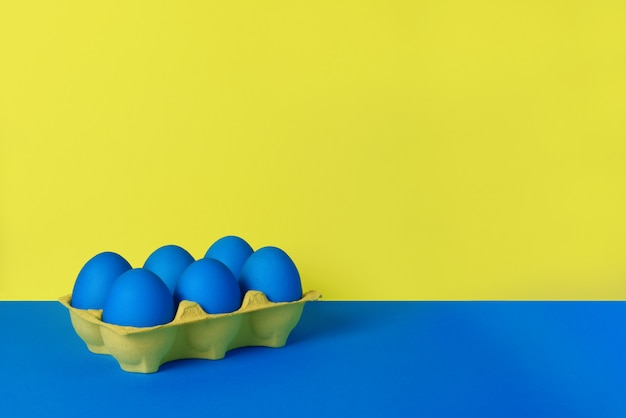 Seis huevos de Pascua pintados de azul en envoltura amarilla sobre fondo azul y amarillo