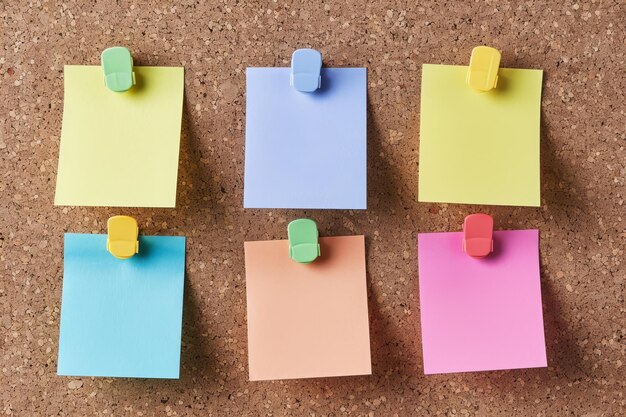 Foto seis notas en blanco de colores pastel están fijadas cuidadosamente a una tabla de corcho marrón