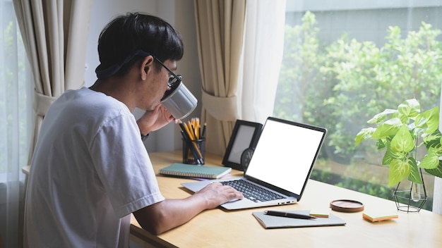 Seitenansicht asiatischer mann, der kaffee trinkt und online auf dem laptop im internet surft