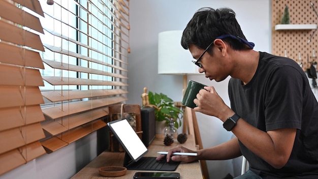 Seitenansicht asiatischer mann, der morgens kaffee trinkt und e-mails auf dem computertisch checkt
