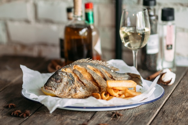 Seitenansicht auf gebratenem Dorado-Fisch mit Pommes Frites und Weißwein